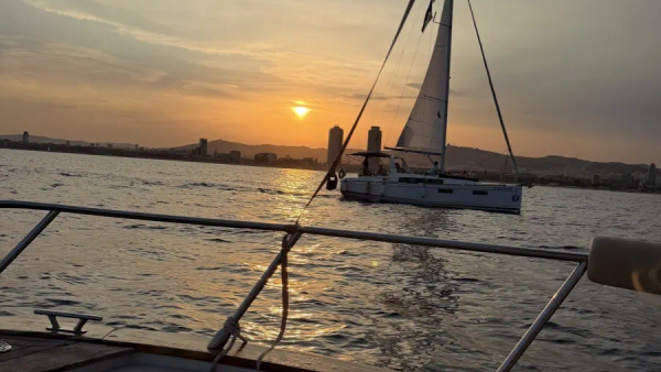 Atardecer desde un barco de alquiler frente a Barcelona, un velero pasando delante del skyline