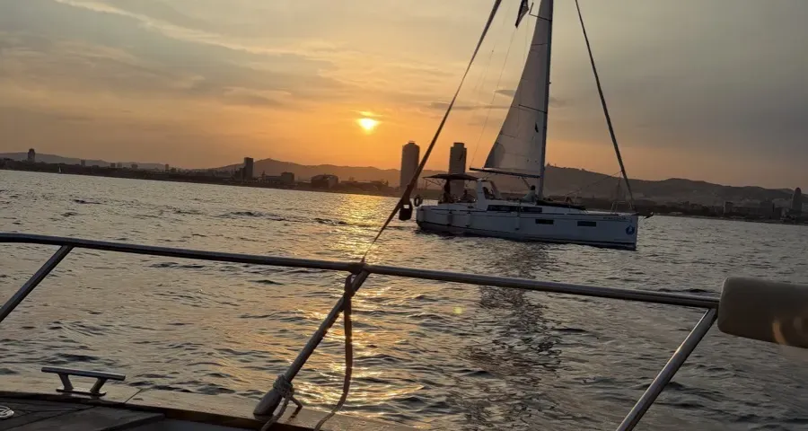 Atardecer desde un barco de alquiler frente a Barcelona, un velero pasando delante del skyline