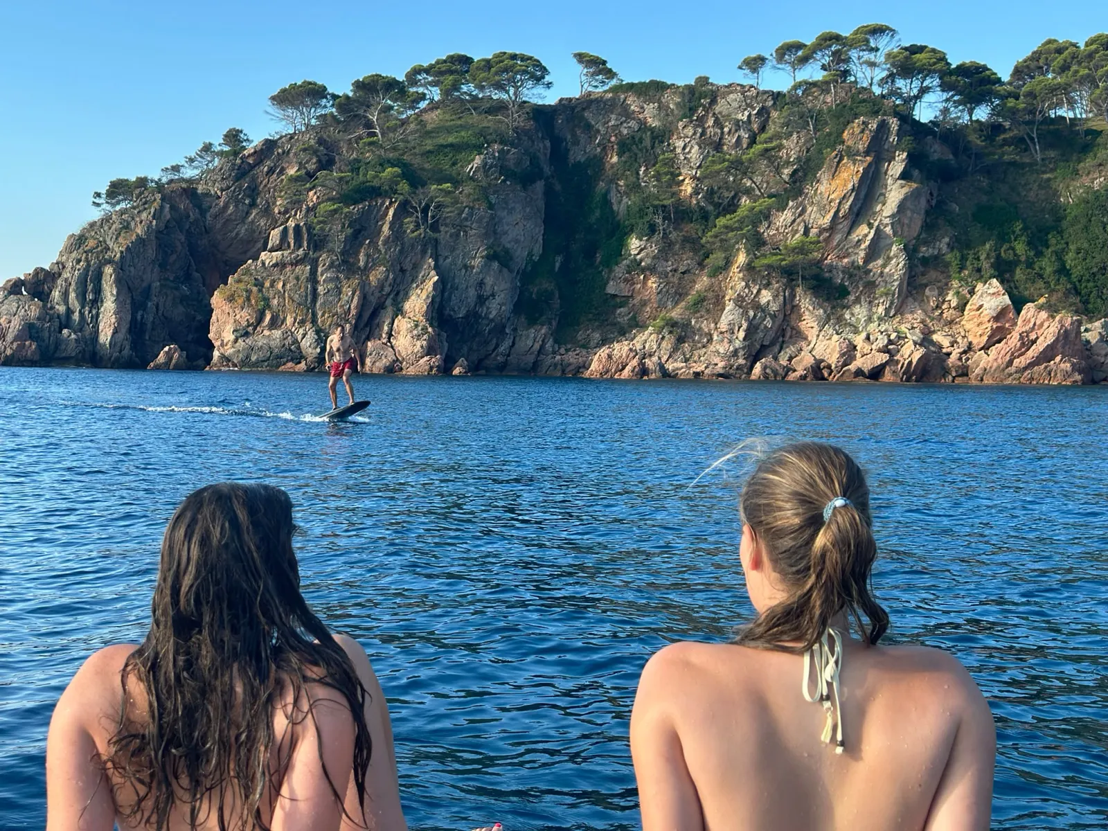 Grupo observando desde el barco a un rider de e-foil junto a los acantilados de Llafranc